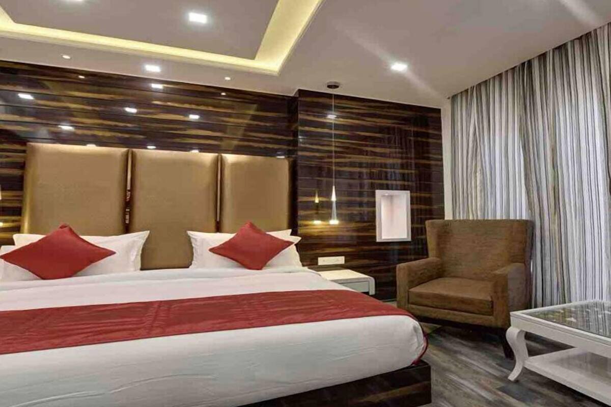 Una habitación de hotel moderna con una cama grande, un sillón marrón y una mesa de centro de vidrio.