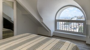 A bedroom with a large arched window, a bed with striped bedding, and a staircase leading to an upper level. - Cosy apartment for 4 people with A/C, WIFI, TV and terrace (Arcachon)