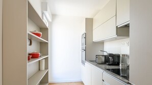 A narrow kitchen with white cabinets, a wooden floor, and a red pot on the shelf. - Cosy apartment for 4 people with A/C, WIFI, TV and terrace (Arcachon)
