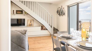 A modern kitchen with a built-in TV, a dining area with a table set for two, and a staircase leading to a loft. - Cosy apartment for 4 people with A/C, WIFI, TV and terrace (Arcachon)