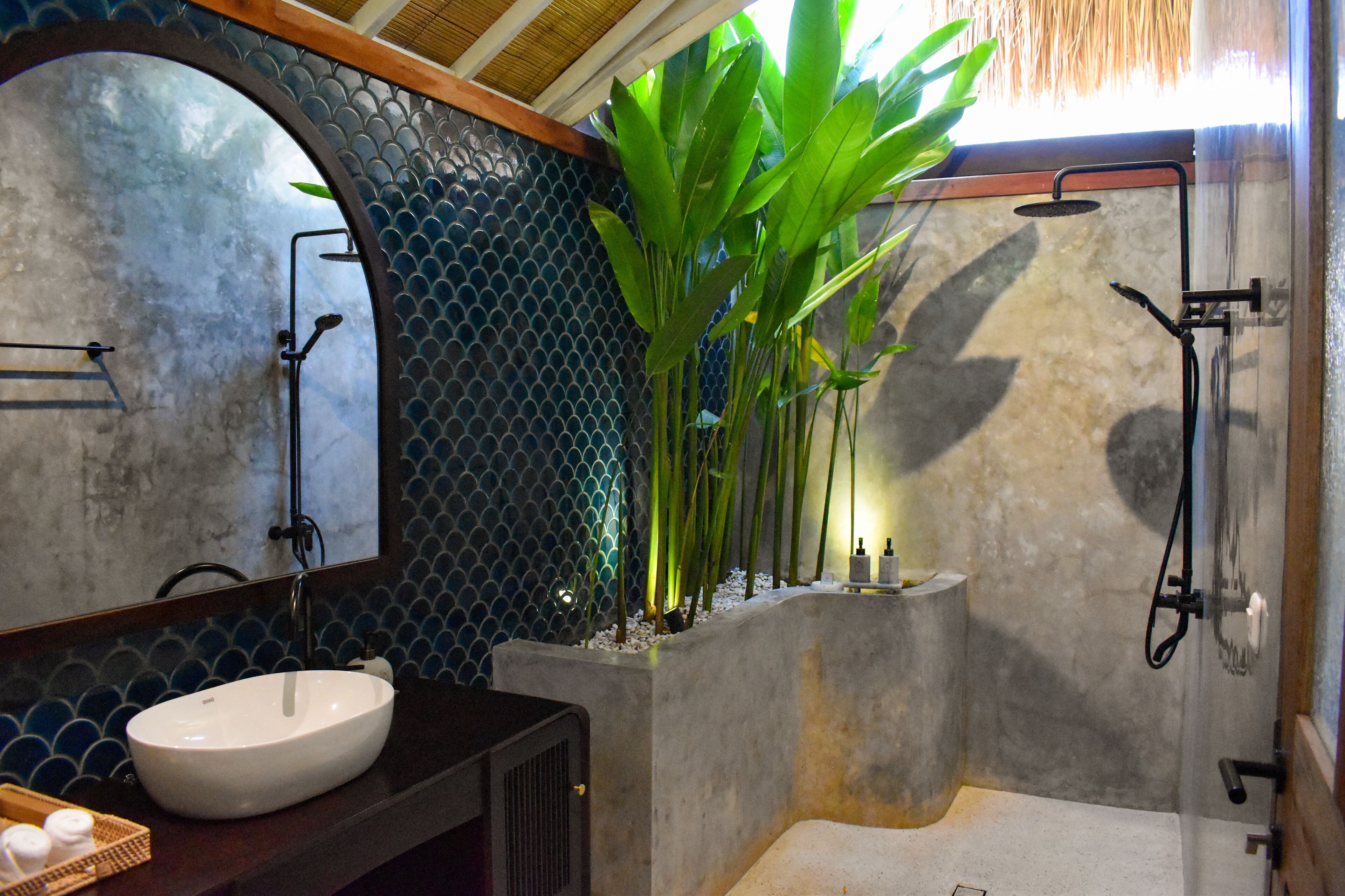 A bathroom with a white sink, a large mirror, a shower, and a potted plant.
