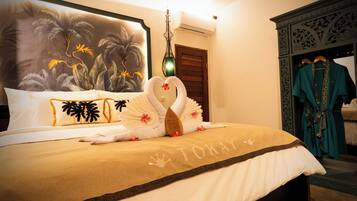 A neatly made bed with a towel swan, a tropical mural, and a teal robe hanging on a rack.