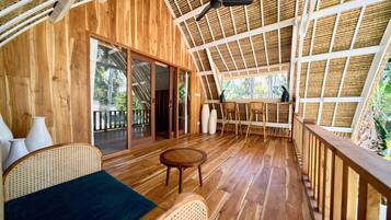 Un interior de madera con ventilador de techo, un amplio ventanal corredero, mobiliario de mimbre y vistas al exterior.