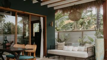 A room with a wooden ceiling, a sofa with cushions, a dining table with chairs, and a large plant in a vase.