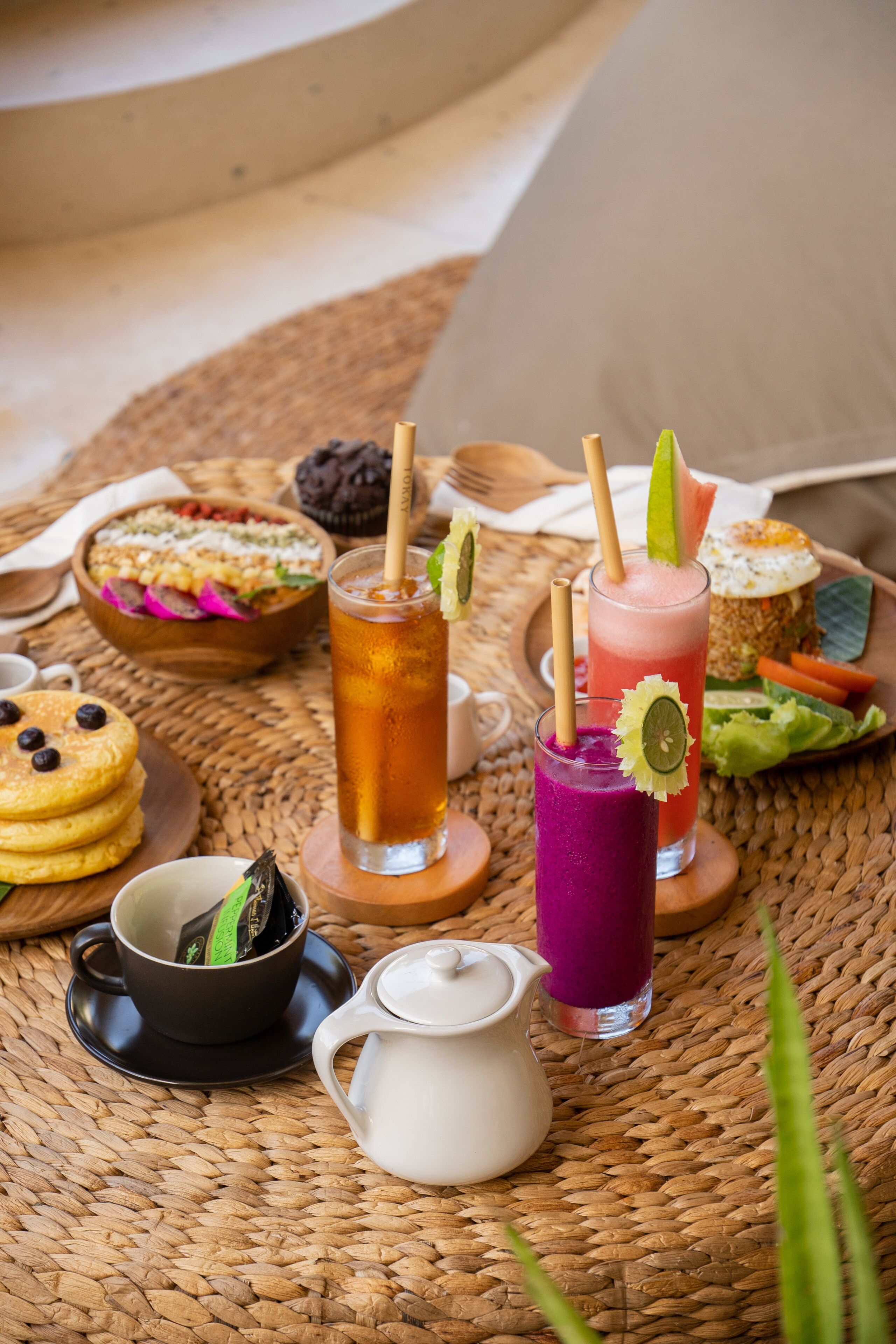 A table with various food items and drinks, including pancakes, a bowl of salad, and two colorful drinks with garnishes.