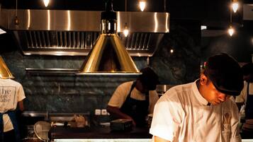 A chef in a professional kitchen with stainless steel appliances and pendant lighting.