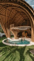 Zona de piscina con estructura de bambú en lo alto, piscina circular y área de descanso con mesas y sillas.