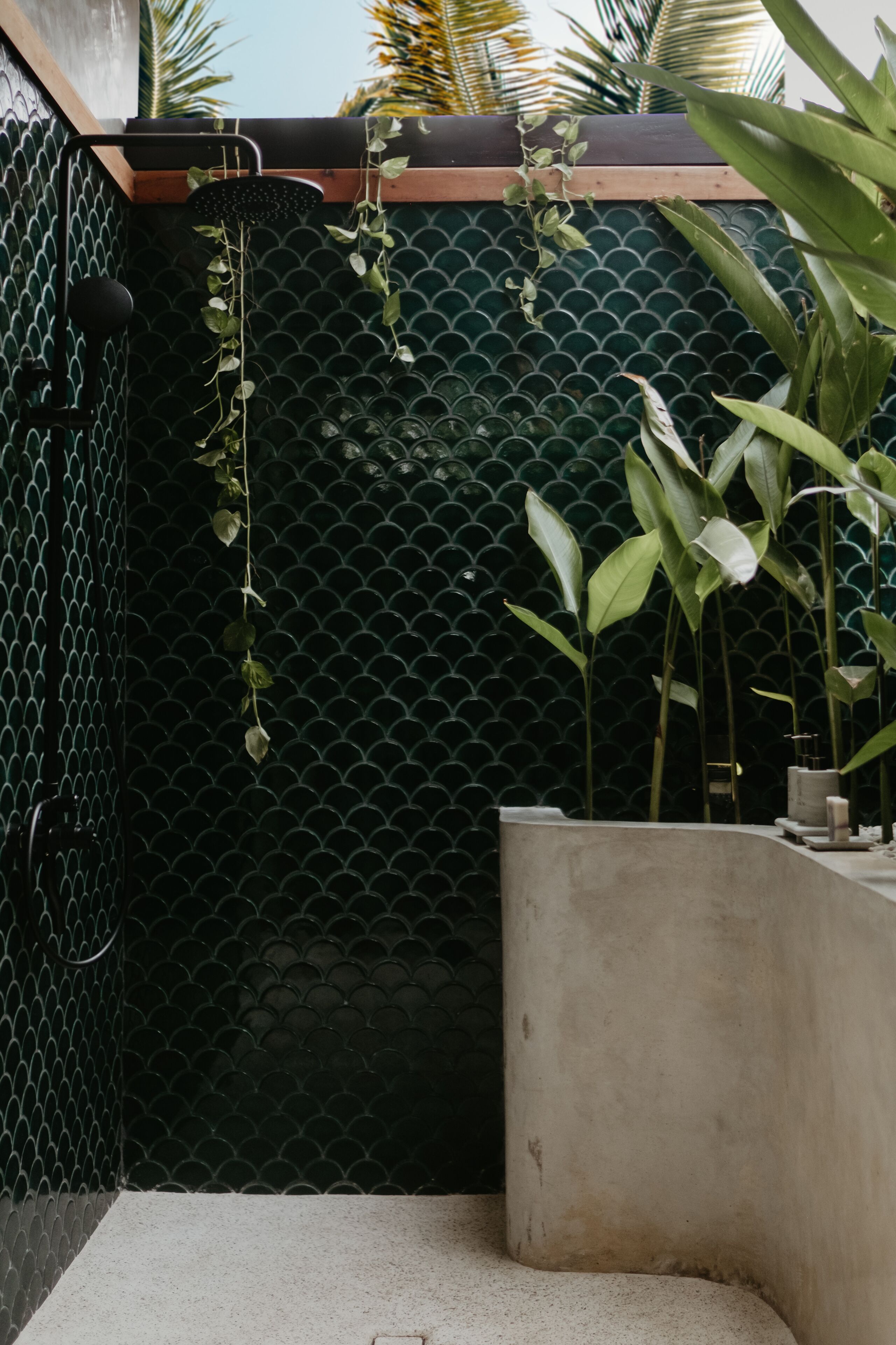 Un área de ducha con pared de azulejos verdes, un banco de hormigón y plantas colgantes.