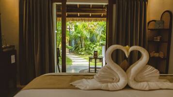 A bed with two swan-shaped towels, a small table, and a view of a tropical garden through a doorway.