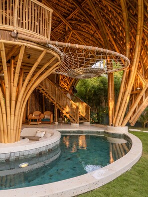 Un área de piscina con una estructura de bambú, una hamaca y una escalera.