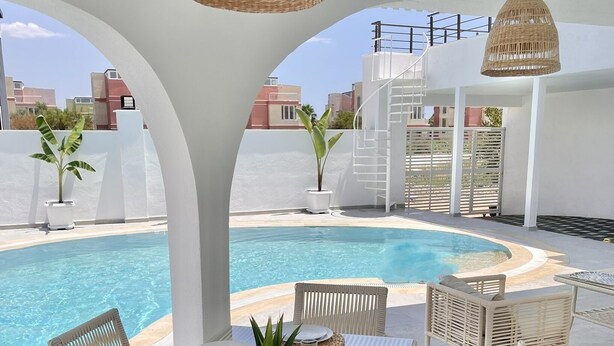 Un área de comedor junto a la piscina con mobiliario de mimbre y vista al agua.