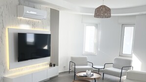 Una sala de estar moderna con un televisor de pantalla plana grande montado en una pared de mármol, dos sofás blancos, una mesa de centro y una lámpara colgante.