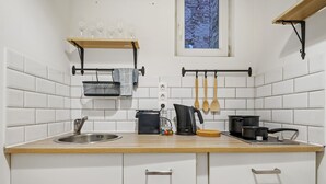 Cozinha com paredes em azulejo branco, bancada de madeira, pia de aço inoxidável, cafeteira e utensílios de cozinha pendurados.