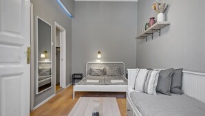 Quarto com cama, mesas de cabeceira, prateleira com objetos decorativos e uma porta.