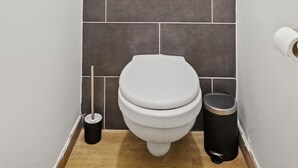 Uma casa de banho pequena e moderna, com uma sanita branca, um caixote de lixo preto e uma janela sobre a sanita.