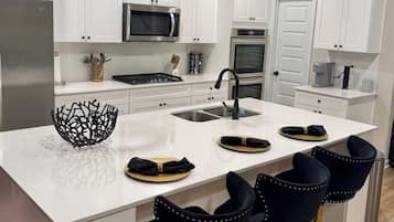 A modern kitchen with white cabinetry, stainless steel appliances, a central island with bar stools, and pendant lighting.