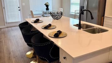 A modern kitchen with a central island, bar stools, a refrigerator, and pendant lighting.