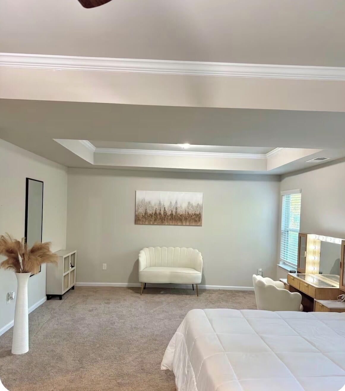 Une chambre à coucher avec un lit, une coiffeuse avec des lampes, une chaise, un tableau au mur et un luminaire au plafond.