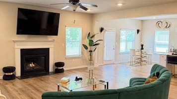 A spacious living room with a green sofa, a fireplace, a ceiling fan, and a flat-screen TV.