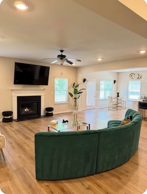 A spacious living room with a green sofa, a fireplace, a ceiling fan, and a flat-screen TV. - Modern 4 bedrooms Luxury Home (Atlanta)