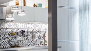 Une cuisine moderne avec un mur arrière décoré de motifs, des armoires blanches et un coin repas comprenant une table et des chaises.