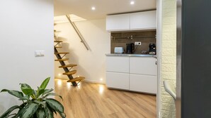 Une cuisine moderne avec des meubles blancs, un escalier en bois et une plante en pot.