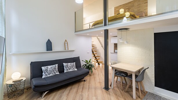 Un appartement moderne de style « loft », avec un canapé noir, une table à manger et un escalier menant à un niveau supérieur.