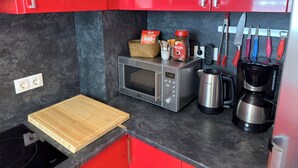 A compact kitchen with red cabinets, a microwave, a coffee maker, and a knife rack. - Exceptional Sea View – Terrace & Private Parking (ROSAS)