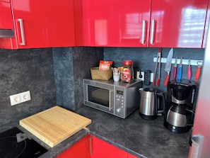 A compact kitchen with red cabinets, a microwave, a coffee maker, and a knife rack.