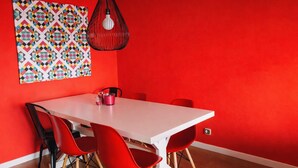 A dining area with a white table, red chairs, a colorful geometric wall art, and a black pendant light. - Exceptional Sea View – Terrace & Private Parking (ROSAS)