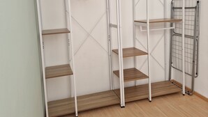 A room with a white wardrobe, wooden shelves, and a metal drying rack.