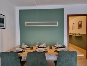 Comedor con mesa de madera dispuesta para seis personas, sillas tapizadas de verde y una pared de acento en tono verde.