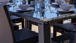 An outdoor dining area with a table set for four, surrounded by wicker chairs, and overlooking a forested hillside.