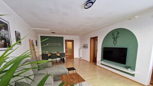A modern living room with a sofa, coffee table, and a TV mounted on a green wall.