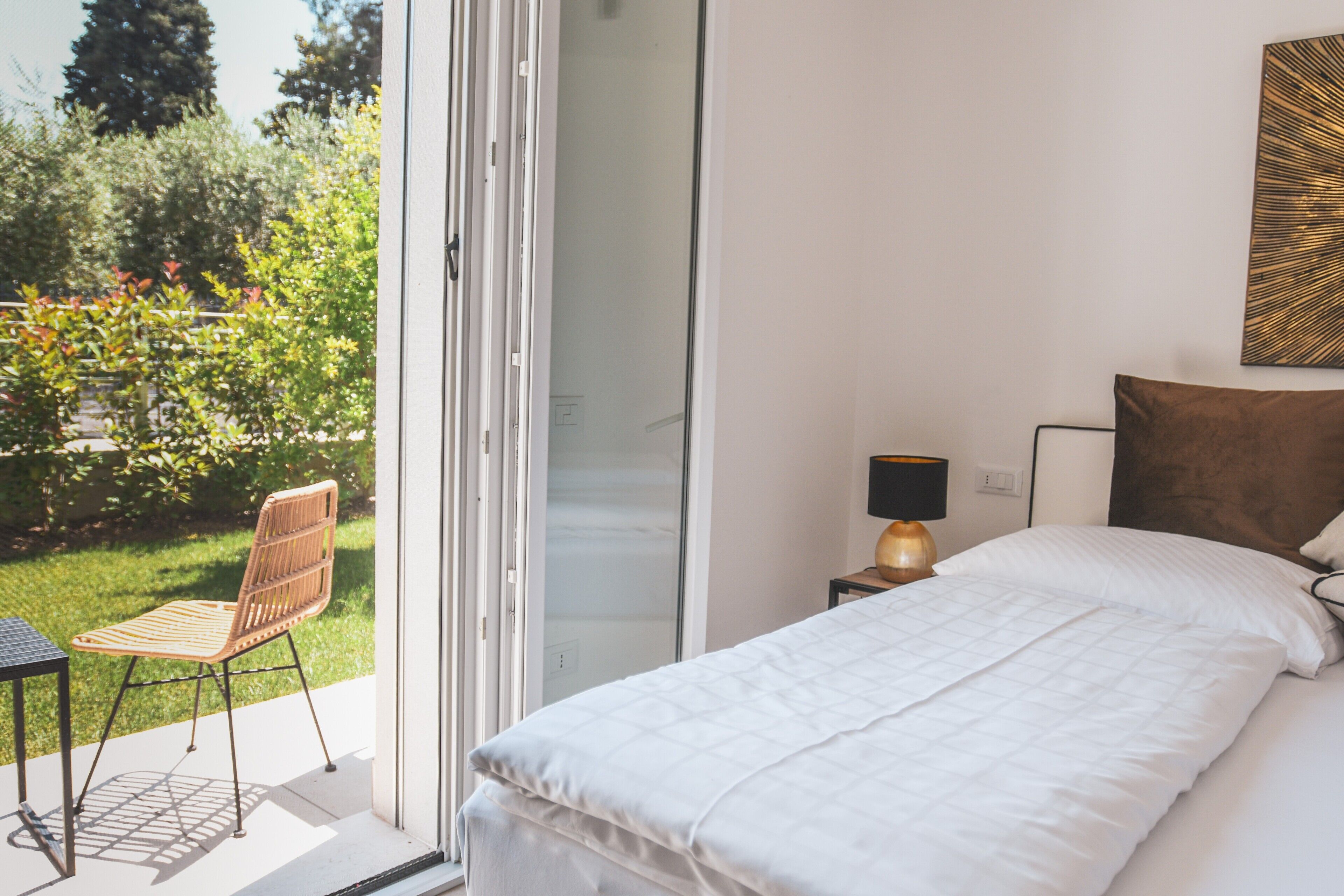 A bedroom with a bed, a chair, a lamp, and a view of greenery outside.