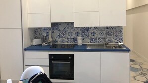 Eine kleine Küche mit weißen Schränken, einer blauen Arbeitsplatte und einer gemusterten Spritzschutzwand.