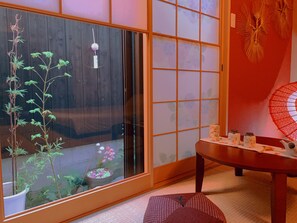 Une pièce de style japonais traditionnel, avec un sol recouvert de tatamis, un paravent shoji, une table en bois avec un service à thé et un bonsaï.