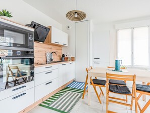 Une cuisine moderne avec des armoires blanches, un four à micro-ondes encastré et un plan de travail en bois. On y trouve un coin repas avec une table et des chaises, ainsi qu’une fenêtre qui laisse entrer la lumière naturelle.