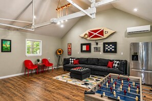Ett vardagsrum i loftstil med ett fotbollsspel, en svart lädersoffa, röda stolar och ett stort fönster.