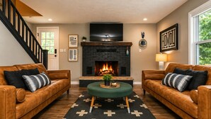 A living room with a fireplace, leather sofas, a coffee table, and a staircase. - Waterfront Renovated Modern A-Frame Hot Tub Game Room Kayaks (Shenandoah)