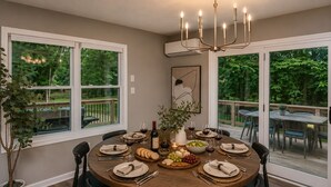 A dining room with a round table set for six, surrounded by chairs, a chandelier, and large windows with a view of the outdoors. - Waterfront Renovated Modern A-Frame Hot Tub Game Room Kayaks (Shenandoah)