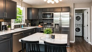 A modern kitchen with dark cabinets, stainless steel appliances, a marble island, and a built-in washing machine. - Waterfront Renovated Modern A-Frame Hot Tub Game Room Kayaks (Shenandoah)