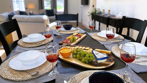A dining table set with plates, glasses, and a charcuterie board with cheese, grapes, and crackers. - National Seashore/Updated/Game Room~Blue Pearl (Eastham)
