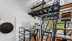 Un loft moderno con una escalera de madera, un comedor con mesa y sillas, y vistas al exterior.