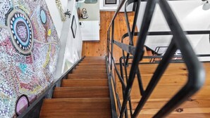 Una escalera de madera con barandilla de metal que conduce a una habitación con un cuadro abstracto y llamativo en la pared y una puerta blanca.