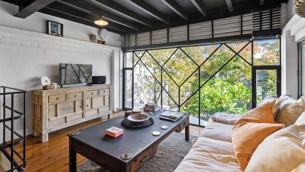Una sala de estar moderna con pared de ladrillo blanco, muebles de madera, un ventanal con vista geométrica y un sofá acogedor.