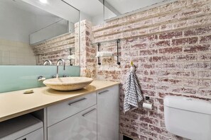 A bathroom with a large round sink, a mirror, and a toilet. The walls are covered with a brick pattern.