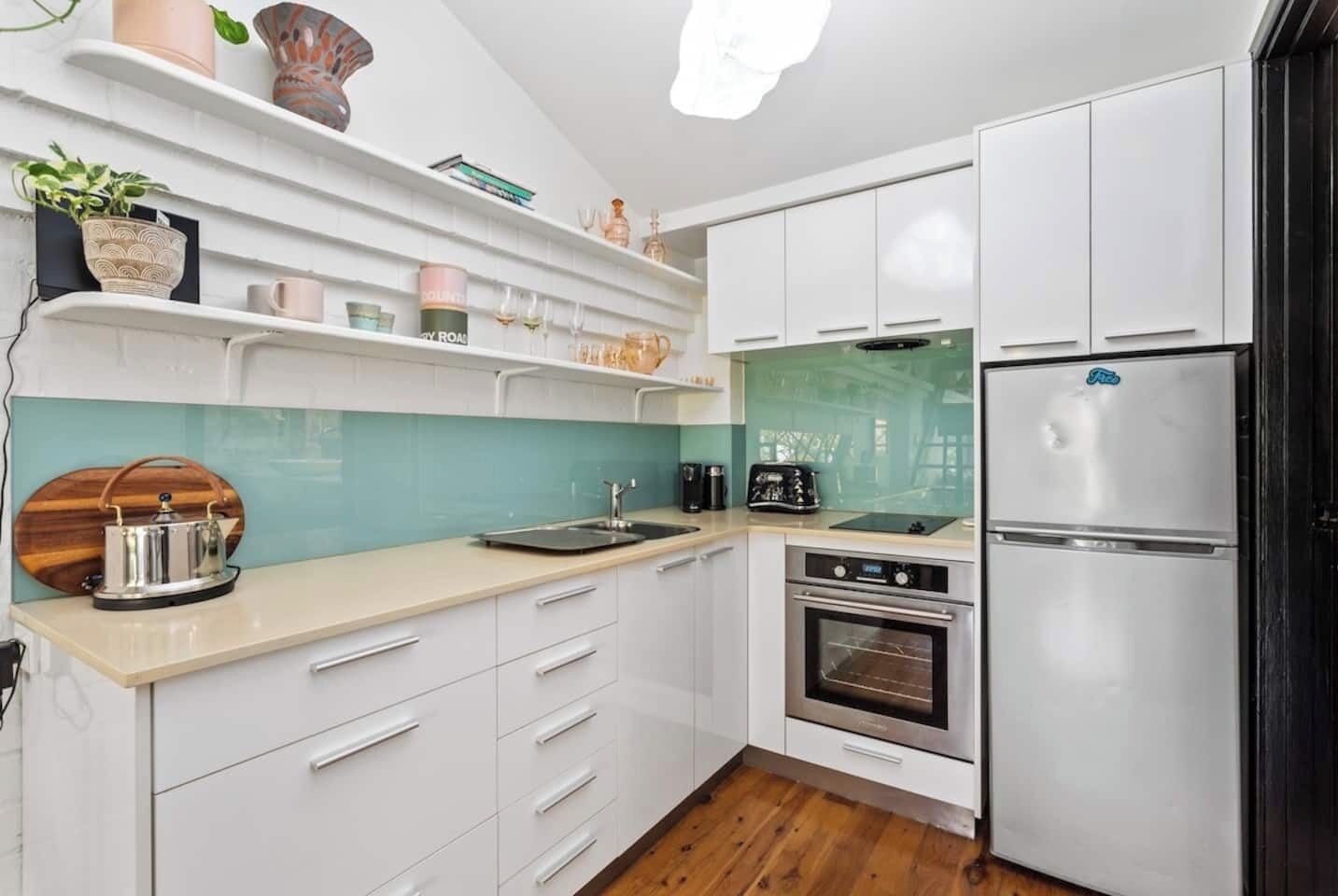 A modern kitchen with white cabinets, a stainless steel refrigerator, a built-in oven, and a teal backsplash.