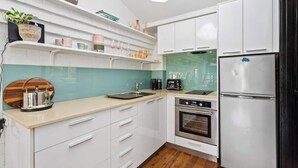 Una cocina moderna con armarios blancos, un refrigerador de acero inoxidable, horno empotrado y salpicadero verde azulado.