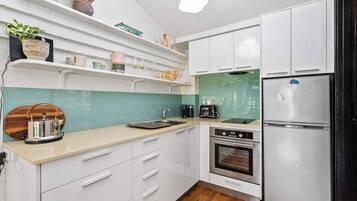A modern kitchen with white cabinets, a stainless steel refrigerator, a built-in oven, and a teal backsplash.